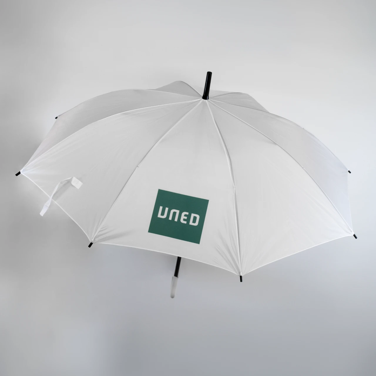 Paraguas blanco con logo UNED en verde sobre fondo claro, abierto y visto desde arriba