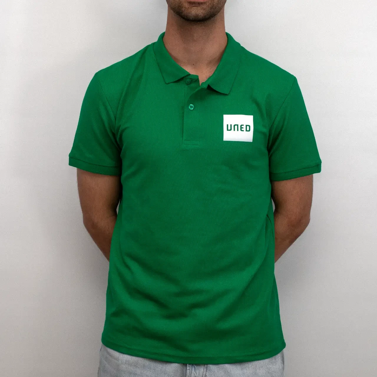 Polo de piqué verde con parche UNED en blanco, vista frontal sobre modelo.