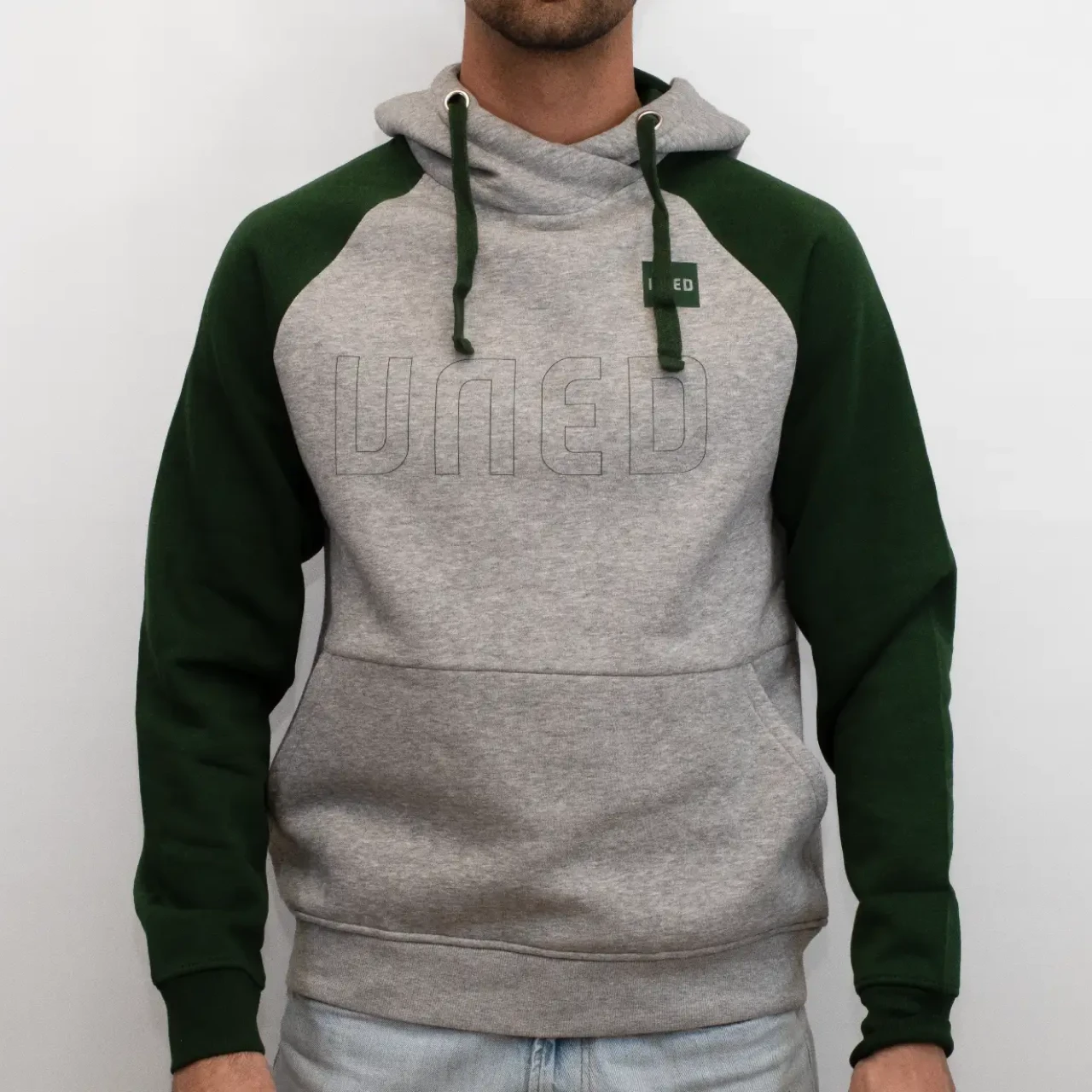 Sudadera bicolor con capucha en gris y mangas raglán en verde con tipografía UNED en el pecho, vista frontal sobre modelo.