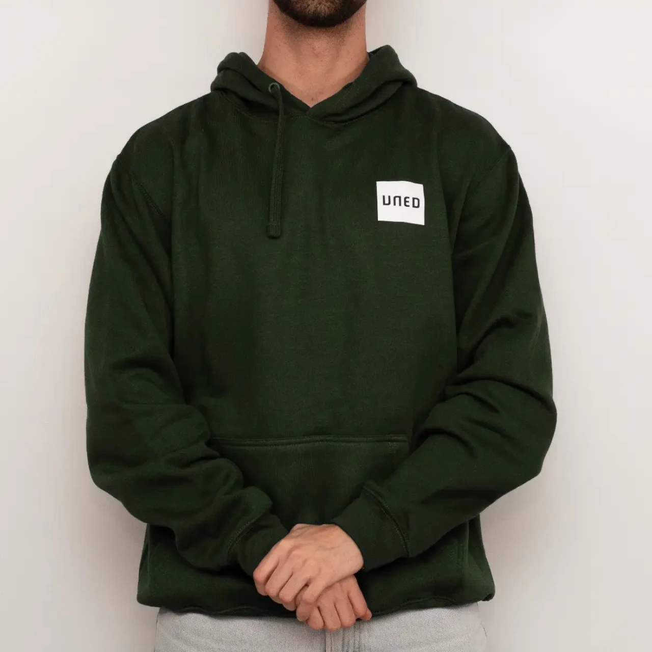 Sudadera con capucha en color verde con parche UNED en crudo, vista frontal completa sobre modelo.