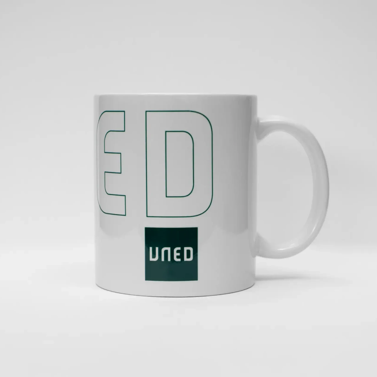 Taza de cerámica blanca con logotipo UNED en verde, vista lateral derecha.
